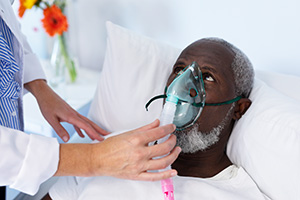 yolo-300x200-83 A caregiver helping an elderly African American man in his bed with an oxygen mask